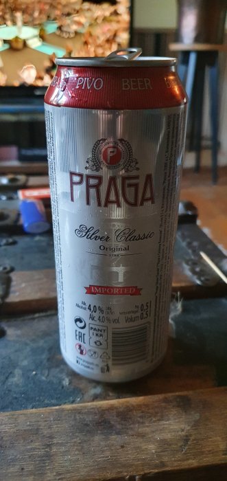 Öppnad ölburk märkt "Praga Pivo Beer" på träbord, suddigt bakgrund.