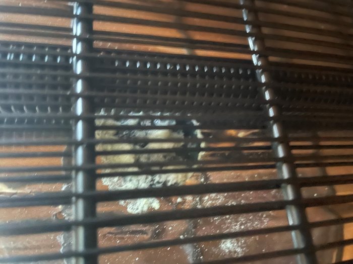 Baksida av kylskåp med vitt skum och misstänkta brännmärken synliga genom galler.