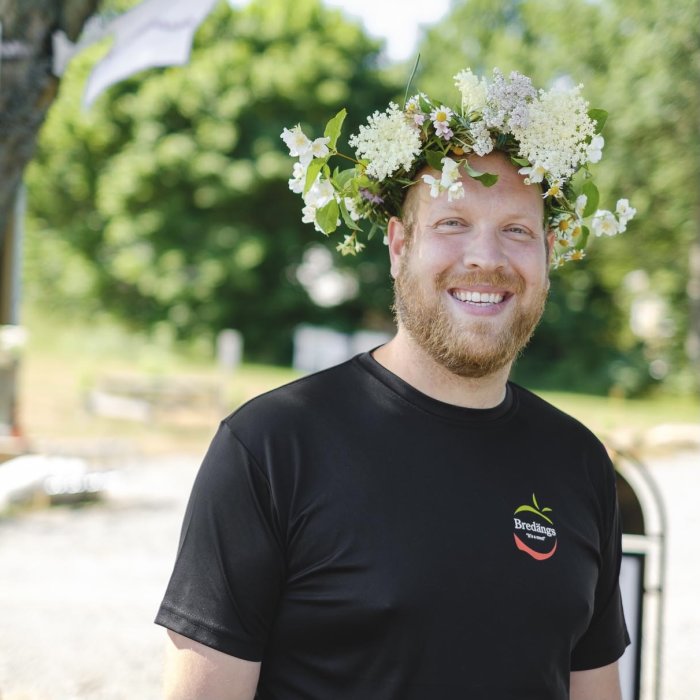 Leende man med blomsterkrans på huvudet firar midsommar i Blekinge.