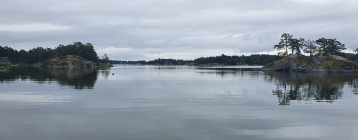 Stilla vattenspegling med skogklädda klippöar under en molnig himmel.