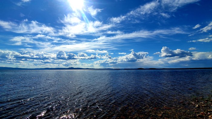 Solig sommarhimmel speglad i havet med några öar i bakgrunden.