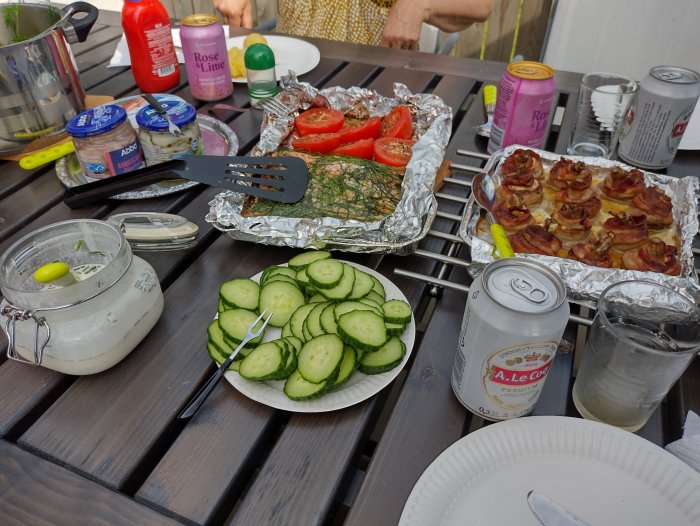 Bord med midsommarmat: sill, knäckebröd, gräddfil, gurka och drycker på en uteservering.