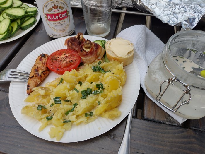 En tallrik med midsommarmat bestående av potatis, grillad kyckling och tomat, intill en burk sill och bröd.