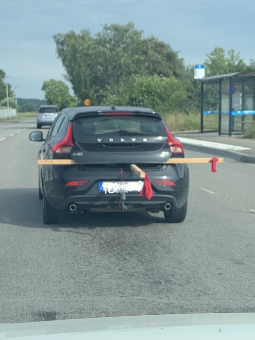 Svart Volvo V40 med en fastbunden trämidsommarstång med röda band sticker ut från bagageutrymmet.