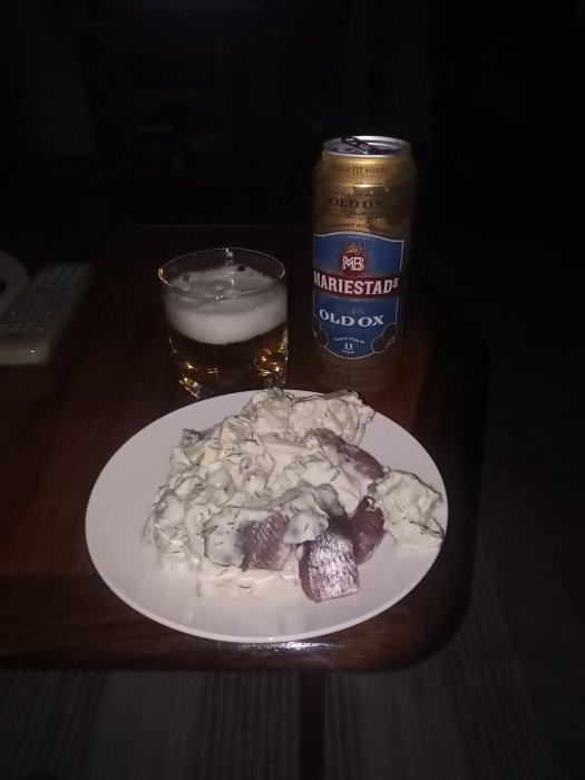 Ölburk bredvid ett glas öl och en tallrik med gubbröra på bord framför TV-fjärrkontroll.