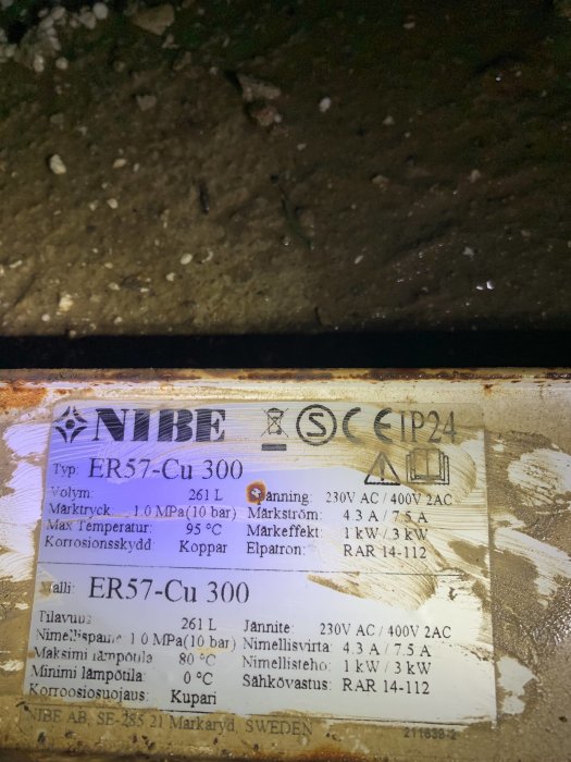 Etikett på en NIBE 300L varmvattenberedare med tekniska specifikationer, synligt slitage och fuktfläckar i bakgrunden.