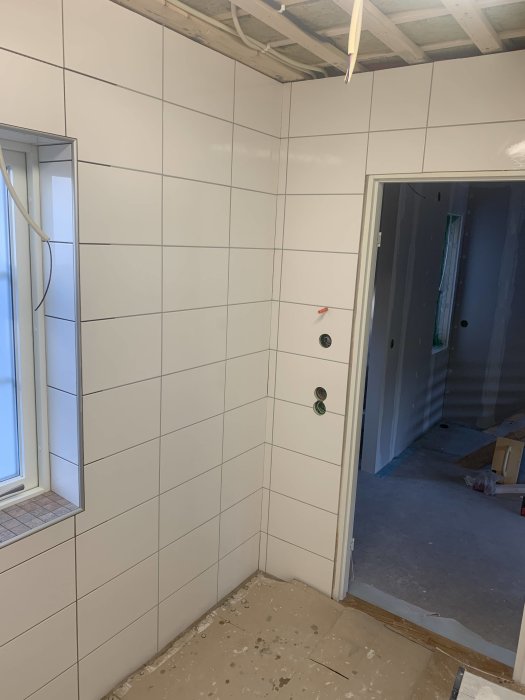 Nyfogade vita kakelväggar i ett badrum under renovering, en vägg och golv återstår.