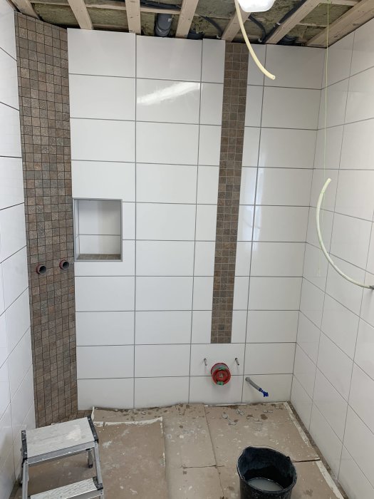 En pågående badrumsrenovering med halvfärdiga kakelväggar och verktyg på golvet.