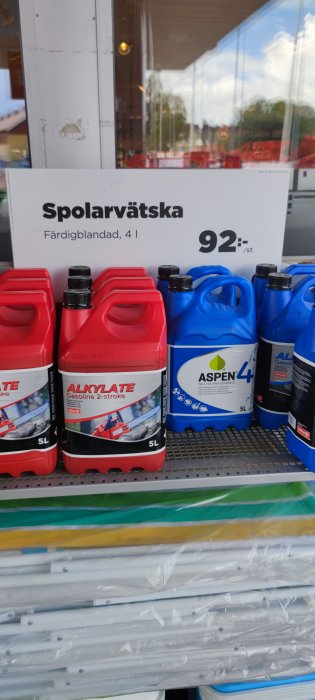 Röda och blåa dunkar med spolarvätska och alkylatbensin framför en bygghandelsskylt.