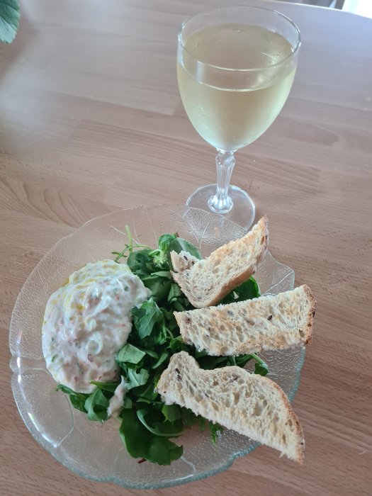 Hemmagjord tzatziki på en bädd av grönt, med rostade brödbitar och ett glas vitt vin på träbord.