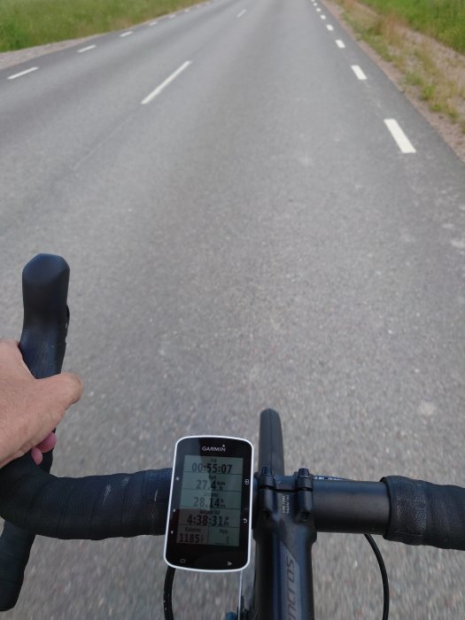 Cyklists perspektiv med cykelstyret och en cykeldator som visar hastighet och distans på en landsväg.