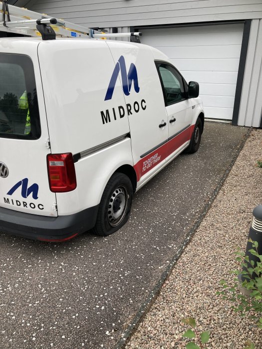 Vit företagsbil parkerad framför en garageport med firmanamnet "MIDROC" på sidan.