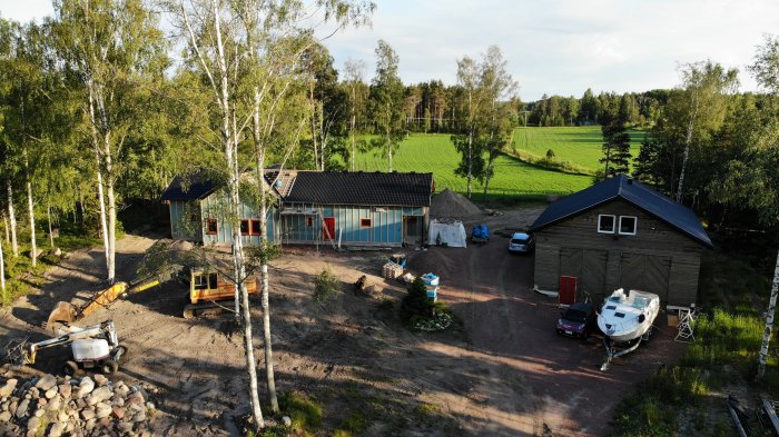 Drönarbild av byggprojekt med halvfärdigt hus, båt på trailer och maskiner på gårdsplan.