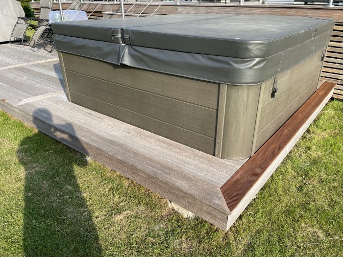 Utomhusbild av ett spabad med täckning på en trädäckplattform i dagsljus.