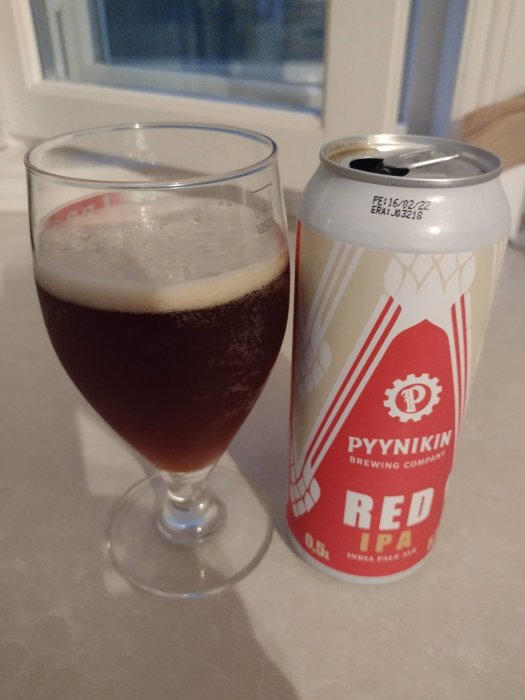 En öppnad burk av Pyynikin Red IPA bredvid ett glas fyllt med mörkröd öl.