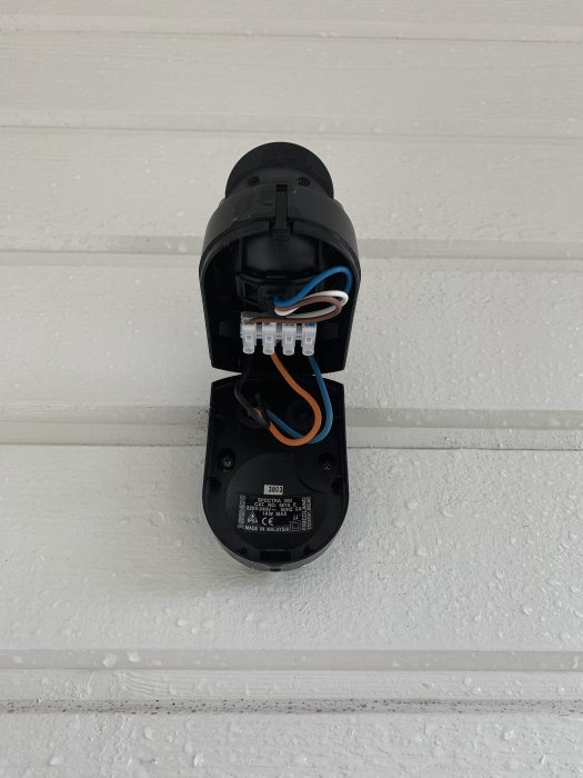 Öppnad svart rörelsevakt monterad på vit vägg visar elektriska kablar och anslutningar inuti.