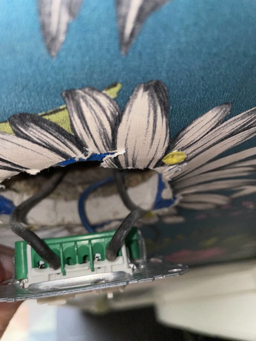 Eluttag med svarta kablar inkopplade och en vit sladd som ligger löst, mot tapet med blommönster.