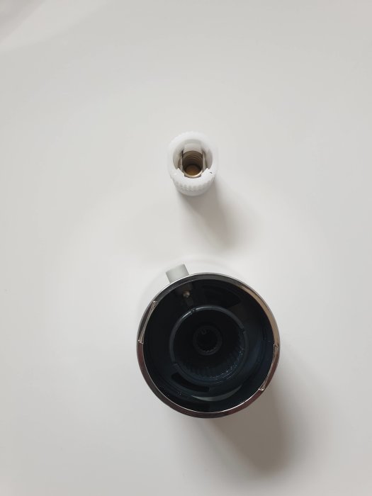 Demonterad blandare med vit plastdel och svart insida på ett vitt underlag.