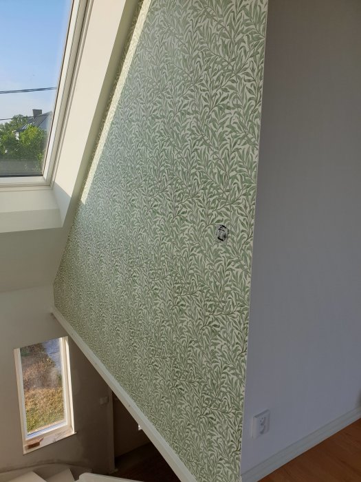 Ny tapet med gröna bladmotiv på en vägg i en trappa med fönster.