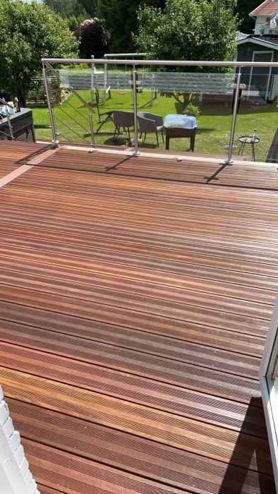 Nyligen oljad träterrass med solsken och trädgårdsmöbler i bakgrunden.