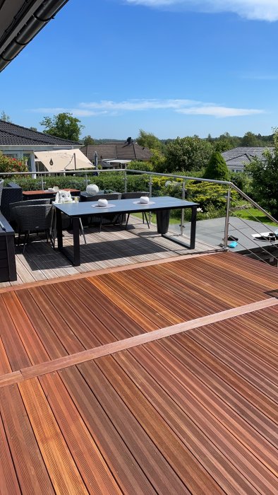 En nymålad terrass med rödbruna plank och utemöbler under en klarblå himmel.