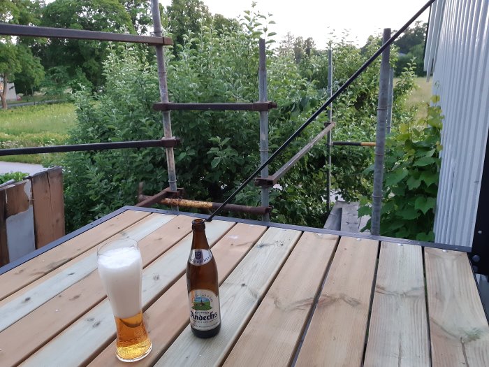 Omonterat balkongräcke och nytt trägolv med en ölflaska och ett glas på balkongen.