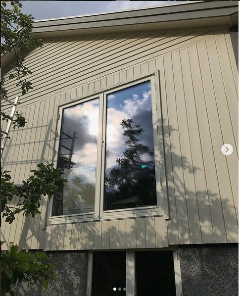 Altan med nyinstallerade fönster och dörrar på ett renoverat 40-tals hus, reflektion av träd och himmel i glaset.