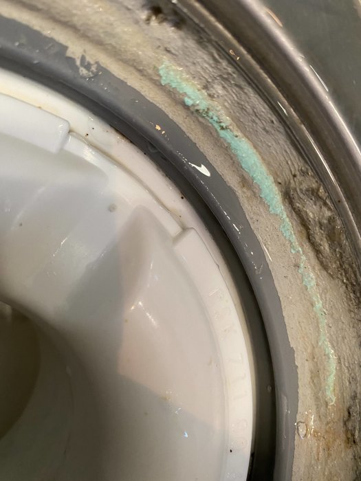 Avloppsrör i golv utan synlig brunnsmanchett, omgiven av våtrumsfolie med mögel och kalkavlagringar.