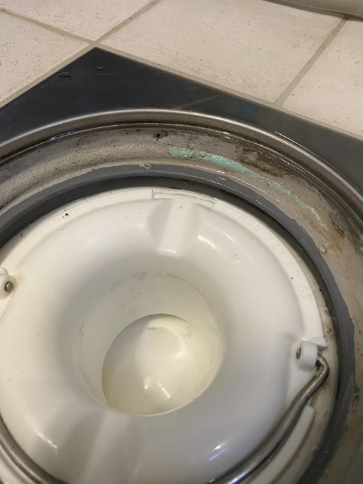 Närbild på ett golvbrunn med synlig våtrumsfolie och avsaknad av brunnsmanchett runt rörets kant.