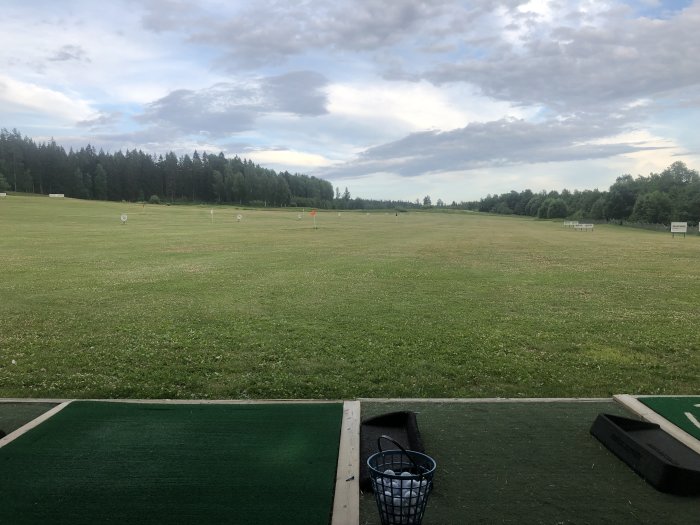 Vy från utslagsplats på driving range med måltavlor på en gräsmatta och skog i bakgrunden.