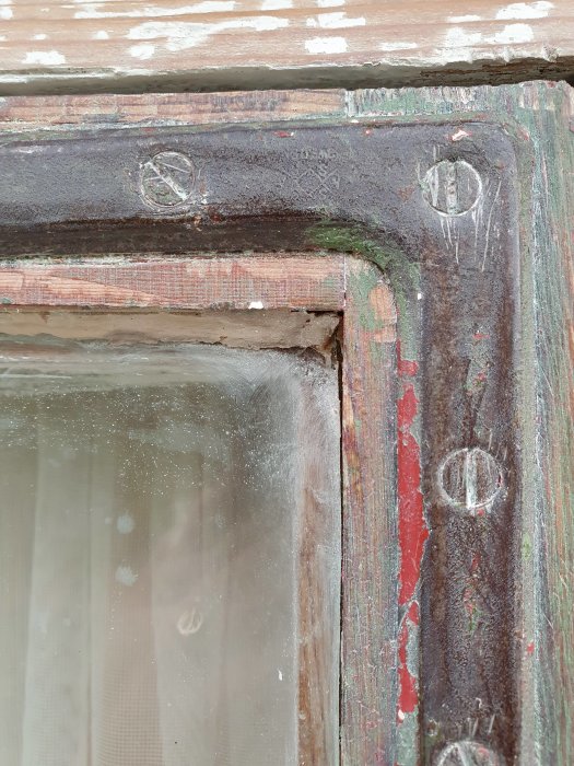 Närbild på fönsterhörn med synliga träpluggar, avskrapat gammalt kitt, och en inoljad yta.