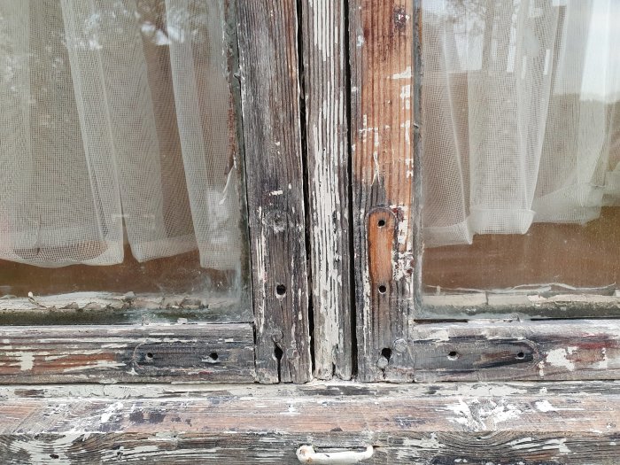 Slitet träfönster med borttaget hörnjärn och spår av gammalt silikonkitt, i behov av renovering.