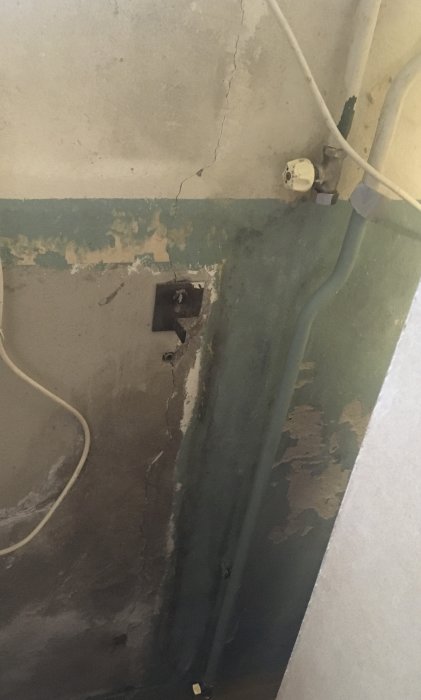 Vägg i källare med borttagen radiator, synliga rördelar och skadad målning.