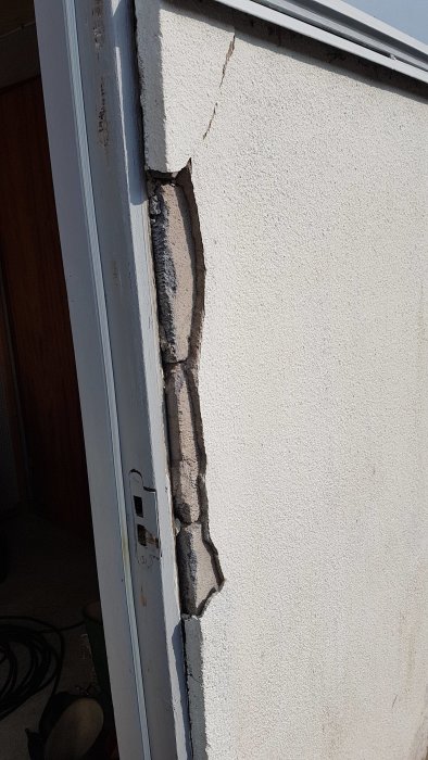 Skadad vägg vid garage med 12 mm tjockt material som har lossnat runt en dörrkarm.