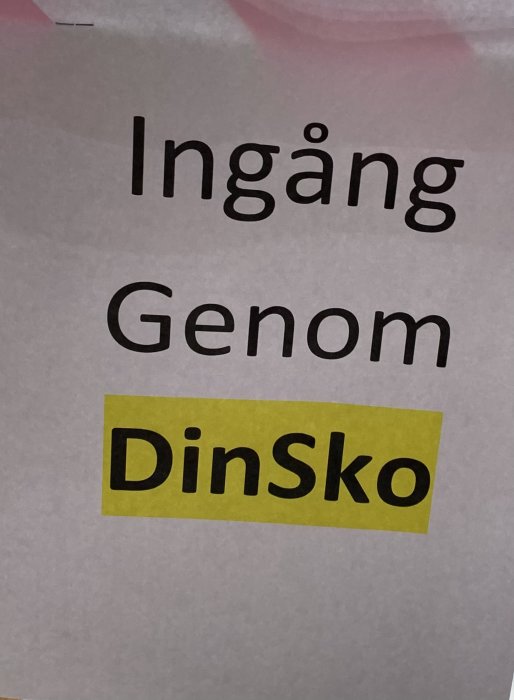 Skylt med texten "Ingång Genom DinSko" i svart och gult på en grå bakgrund.