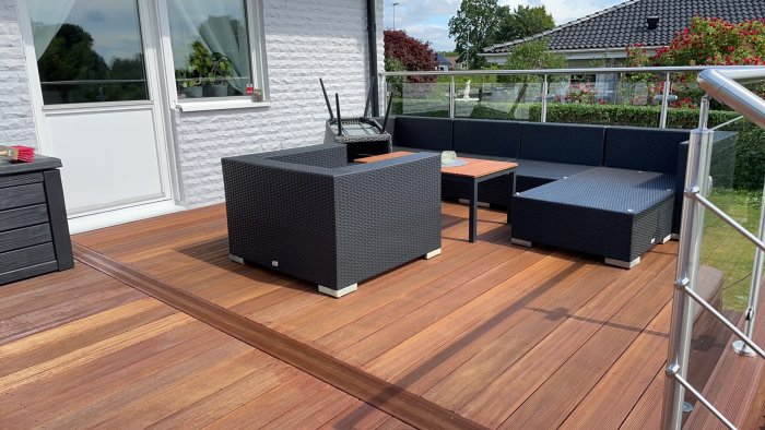 Nybyggd uteplats med trägolv, rottingmöbler och ett glasstaket, ger en inbjudande yta för barfota avkoppling.