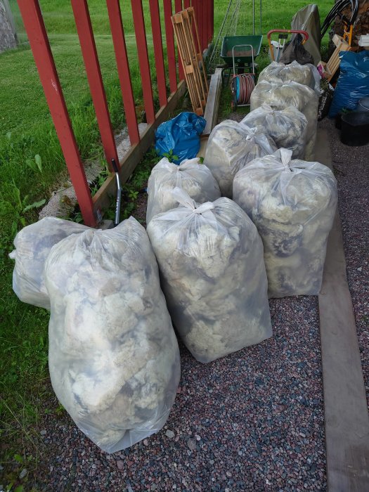 Nio säckar med gammal isolering från takprojekt utomhus bredvid röd trapp.