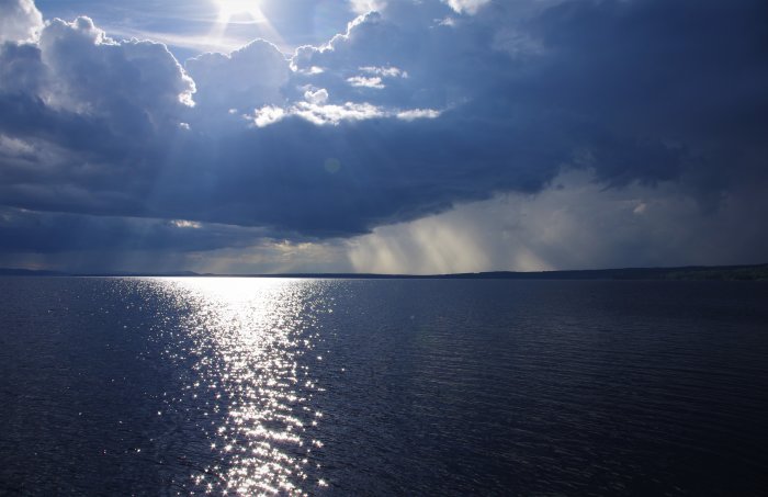 Solas strålar bryter genom molnen och reflekterar över vattenytan.