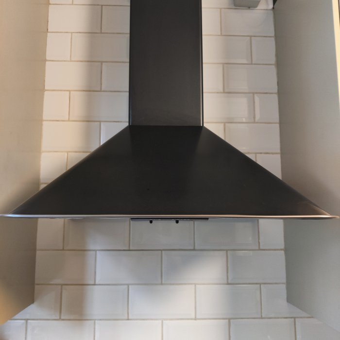 Köksfläkt monterad ovanför spis, mot kaklad vägg, misstänkt att vara en äldre IKEA LUFTIG modell.