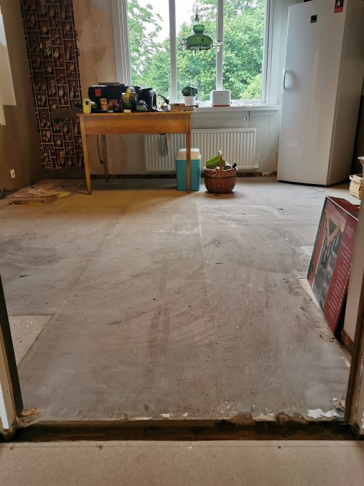 Ett rum under renovering med borttaget golv och synliga limrester samt renoveringsmaterial och verktyg.