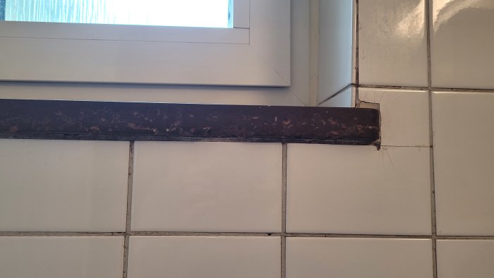 Skadad marmorskiva på fönsterbräda i badrum med spår av vattenskador och lossnande bitar.