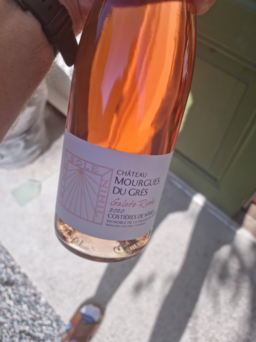 Hand håller en flaska rosévin Chateau Mourgues Du Gres Galets Rosés 2020 med transparent etikett.