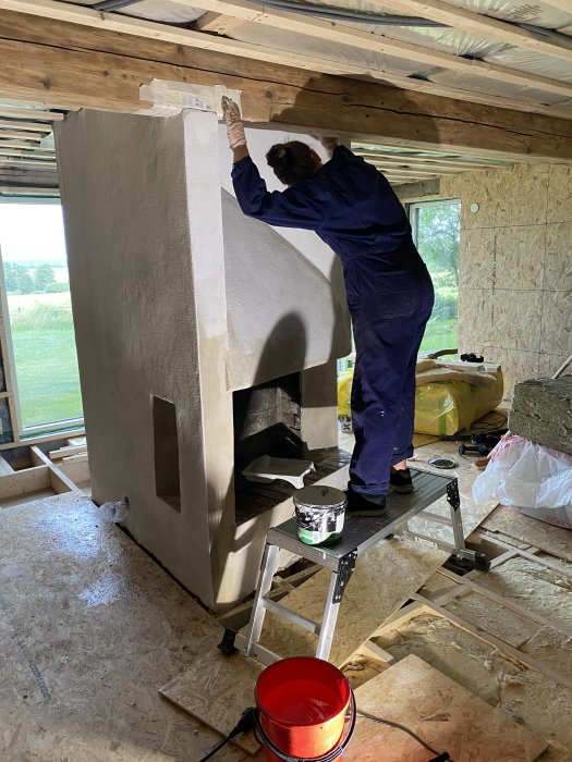 Person målar en nyligen putsad öppen spis under en renovering.