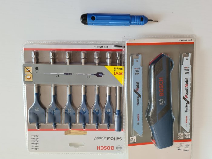 Bitsats med olika storlekar bredvid en blå skruvmejsel och förpackningar med sticksågsblad.