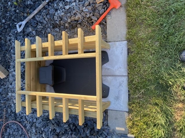 Robotic lawn mower charging station with guide wires on a freshly laid patio, bordered by grass and stones.