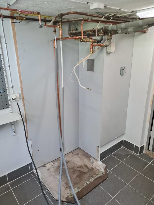 Vägg delvis rivet med exponerade rör och elkablar där en värmepump tidigare demonterats.