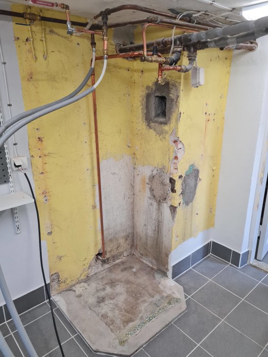 Rivna väggskivor och exponerade rör i ett rum under renovering.