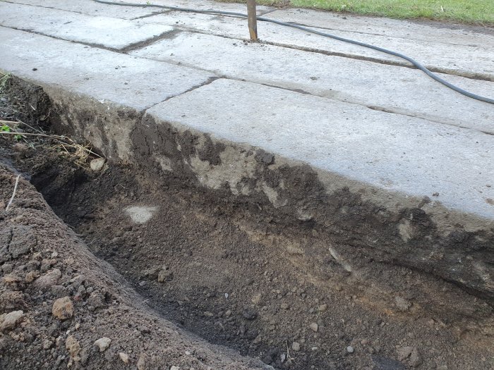 Gråa granitstenblock med slät yta, ca 15 cm tjocklek, som en del av en utgrävd yta.
