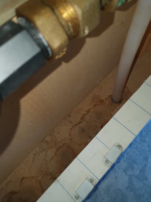 Vattenrör och en PVC-rörstam med misstänkt mögeltillväxt och fuktfläckar på en vägg i ett skåp.