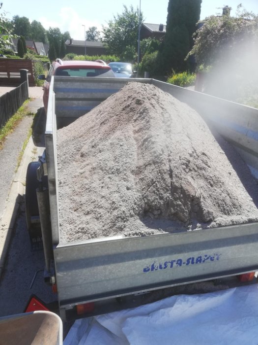 Släpvagn fullastad med grus parkerad på en gata i bostadsområde.